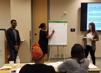 Three people presenting to conference attendees, with a woman writing on a paper easel