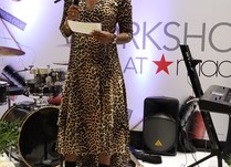 A woman holding a microphone speaking to attendees from a stage