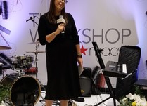 A woman holding a microphone speaking to attendees from a stage