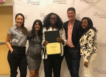 A woman holding a Chen Burkett New York certificate of completion stands with a group posing in front of The Workshop at Macys banner 