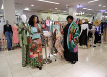 Two women in colorful dresses in front a mannequin and clothing rack