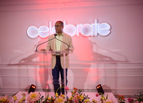 Man speaking at podium in front of celebrate neon sign