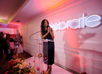 Woman speaking at podium in front of celebrate neon sign