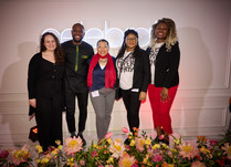 Group of 5 people standing in front of a celebrate neon sign