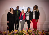 Group of 5 people standing in front of a celebrate neon sign