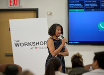 A woman with a microphone addresses the workshop attendees
