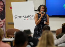 A woman with a microphone addresses the workshop attendees