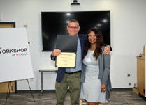 A man presenting a woman with a My Mommy Wisdom Certificate of Completion