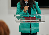 A woman with a microphone addresses the workshop attendees from podium