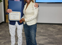 A man presenting a woman with a The Standard Shoes Certificate of Completion