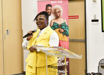 A woman with a microphone speaks the workshop attendees from podium