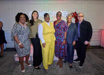 Group of panelists standing in front of "celebrate" neon sign