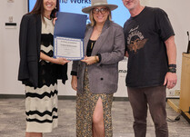 A woman presenting two people with a Naked Rebellion Certificate of Completion