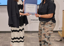 A woman presenting another woman with a School Scents Candles Certificate of Completion