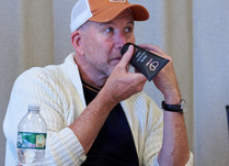 Man sitting at a table, applying a skincare product to his face